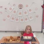 Dziewczynka trzymająca bochenki chleba, z tyłu tablica z napisem 